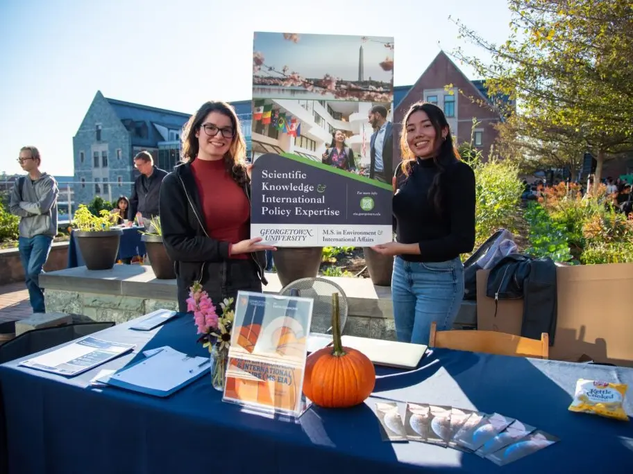 Two students holding up a poster at a booth fair in the fall on campus.